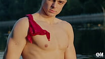 Jovencito tatuado en bikini rojo desnudándose y bañándose en el río